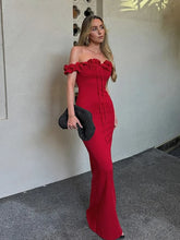 Woman in a red off-shoulder dress holding a black clutch against a neutral wall.